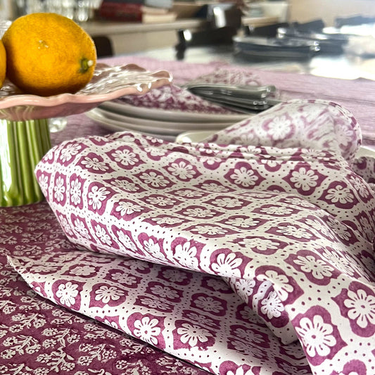 Table setting with a purple floral tablecloth, lemons on a plate, and a folded white and purple patterned napkin.