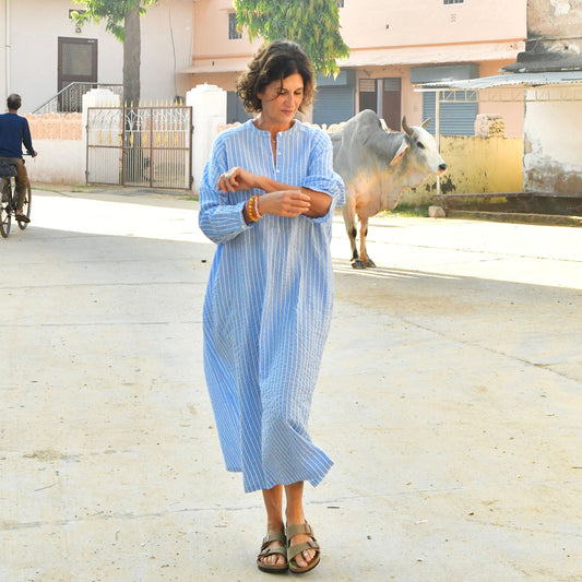 Woman in a blue striped dress standing on a street with a cow in the background
