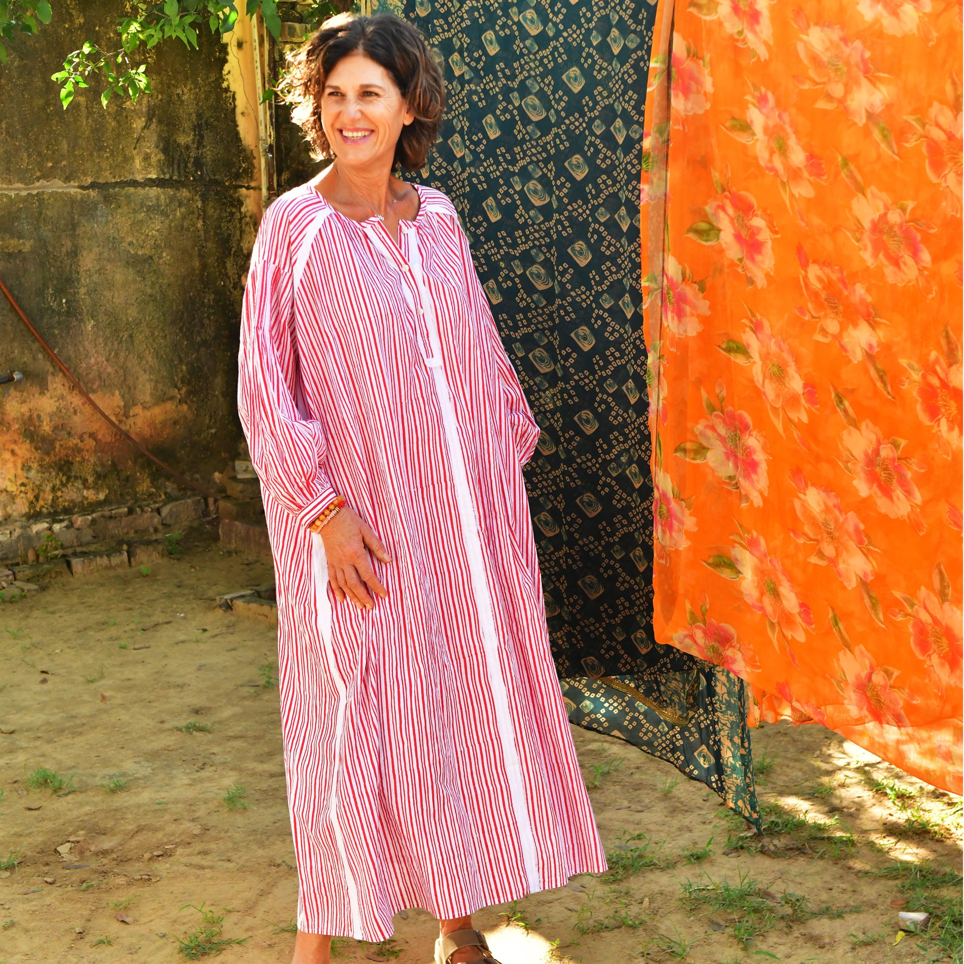 Woman wearing a pink and white striped dress standing in front of colorful fabrics.